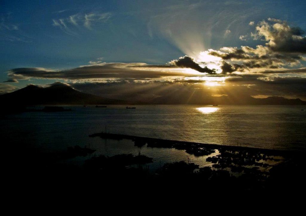 best photo spots in golfo di napoli naples showing a panoramic sunset view of mount vesuvius behind deep blue water layouts