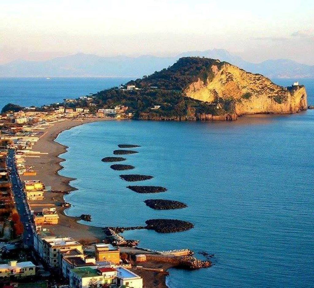 is capo miseno bacoli worth visiting or skip massive vertical yellow volcanic cliffs towering over a quiet turquoise bay